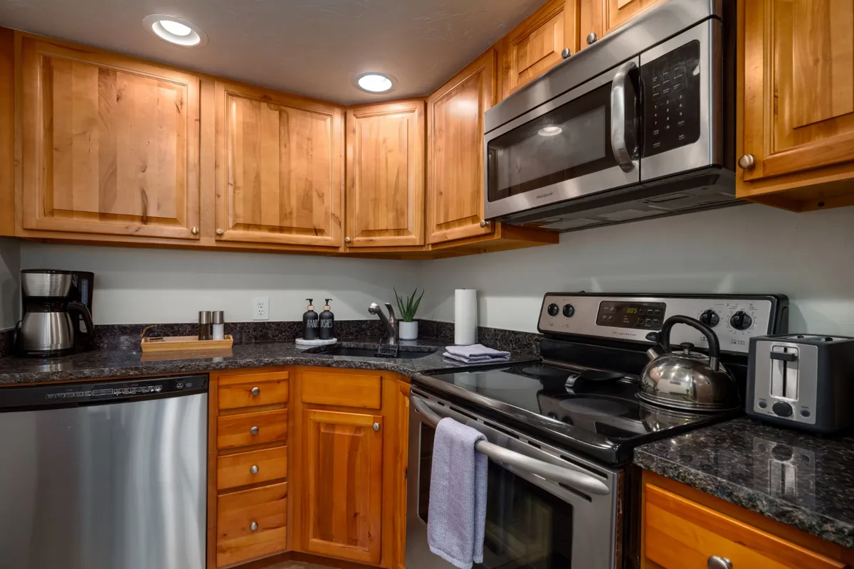 This image showcases a well-lit kitchen featuring stainless steel appliances, sleek granite countertops, and warm wooden cabinetry. A coffee maker and kettle are placed on the counter, suggesting a functional and inviting cooking space.