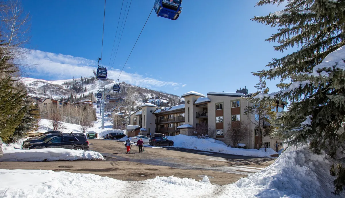 This lively exterior image displays multiple ski gondolas gliding over a snowy landscape with people walking and a striking mountain backdrop. The architecture of nearby buildings and the bustle of visitors create an energetic mountain resort atmosphere.