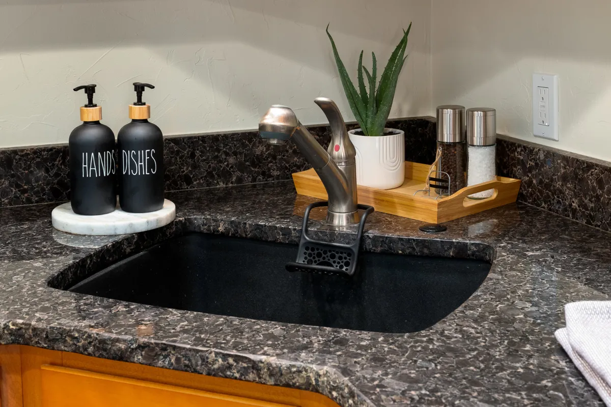 A neatly organized interior space featuring a sink area with soap dispensers, a small plant, and salt and pepper shakers. The inviting setup suggests a communal environment suitable for practical needs like laundry or gear prep.