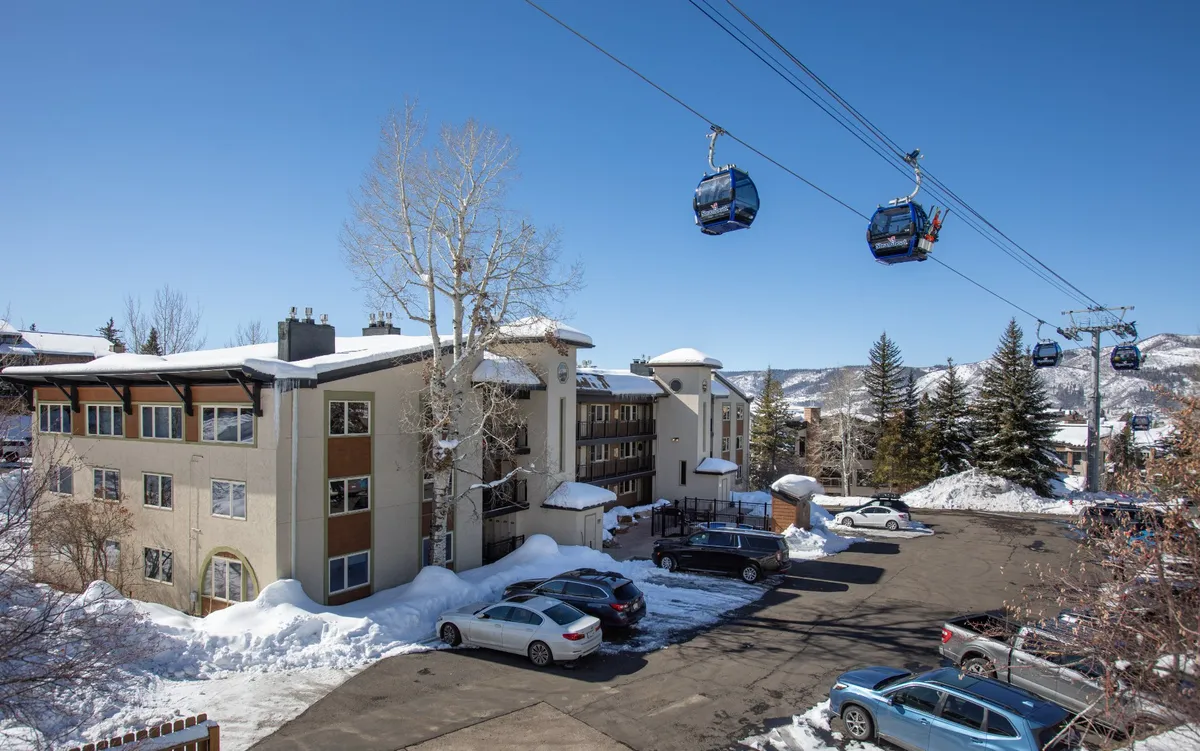 A snow-covered landscape surrounds the building, with gondolas gliding in the background and evergreen trees adding a sense of seclusion. The scene evokes a sense of winter magic, with the mountains and lifts inviting couples to explore the area or enjoy the beauty from the comfort of their retreat.
