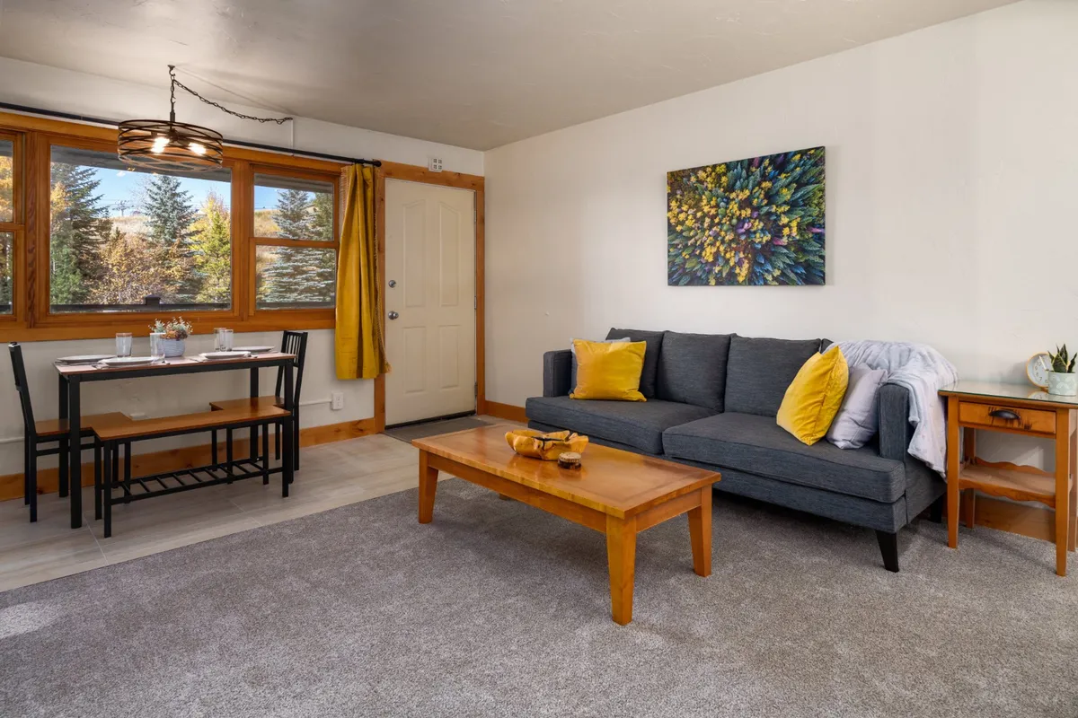 A stylish living area with a comfortable sofa, contemporary artwork, a dining table, and a visible door. The arrangement demonstrates the thoughtful design, offering ample space for both stretching out and hosting social gatherings.