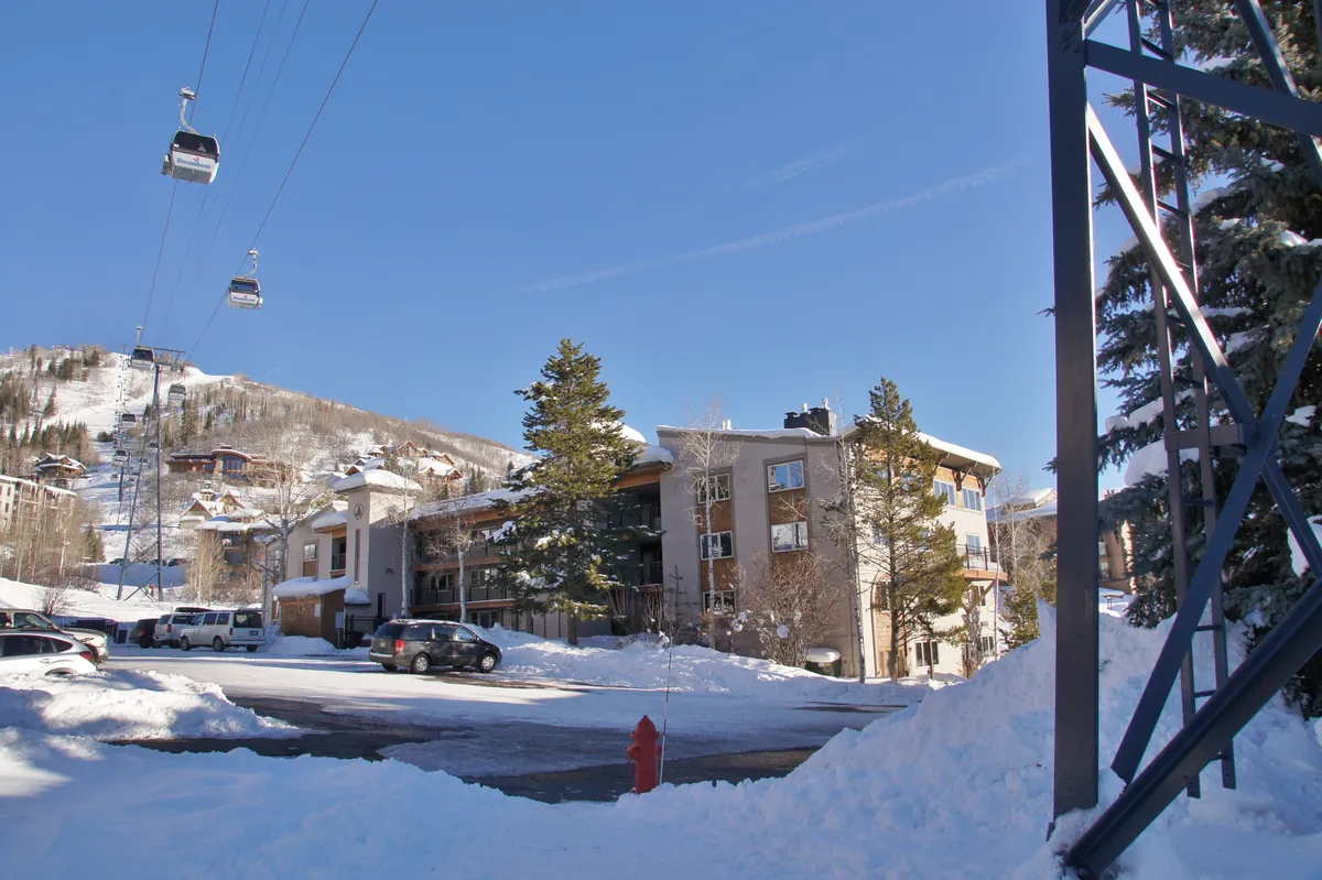 A wintry view of the property facade with snow-covered ground, a visible ski lift, and pine trees, perfectly capturing the seasonal charm of Steamboat. The scene suggests a relaxed yet adventurous lifestyle, right at the edge of outdoor action.